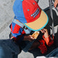 Child wearing a colorful cap eating pizza on a street