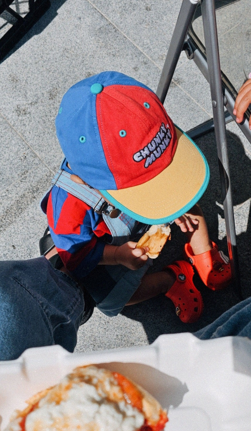Child wearing a colorful cap eating pizza on a street